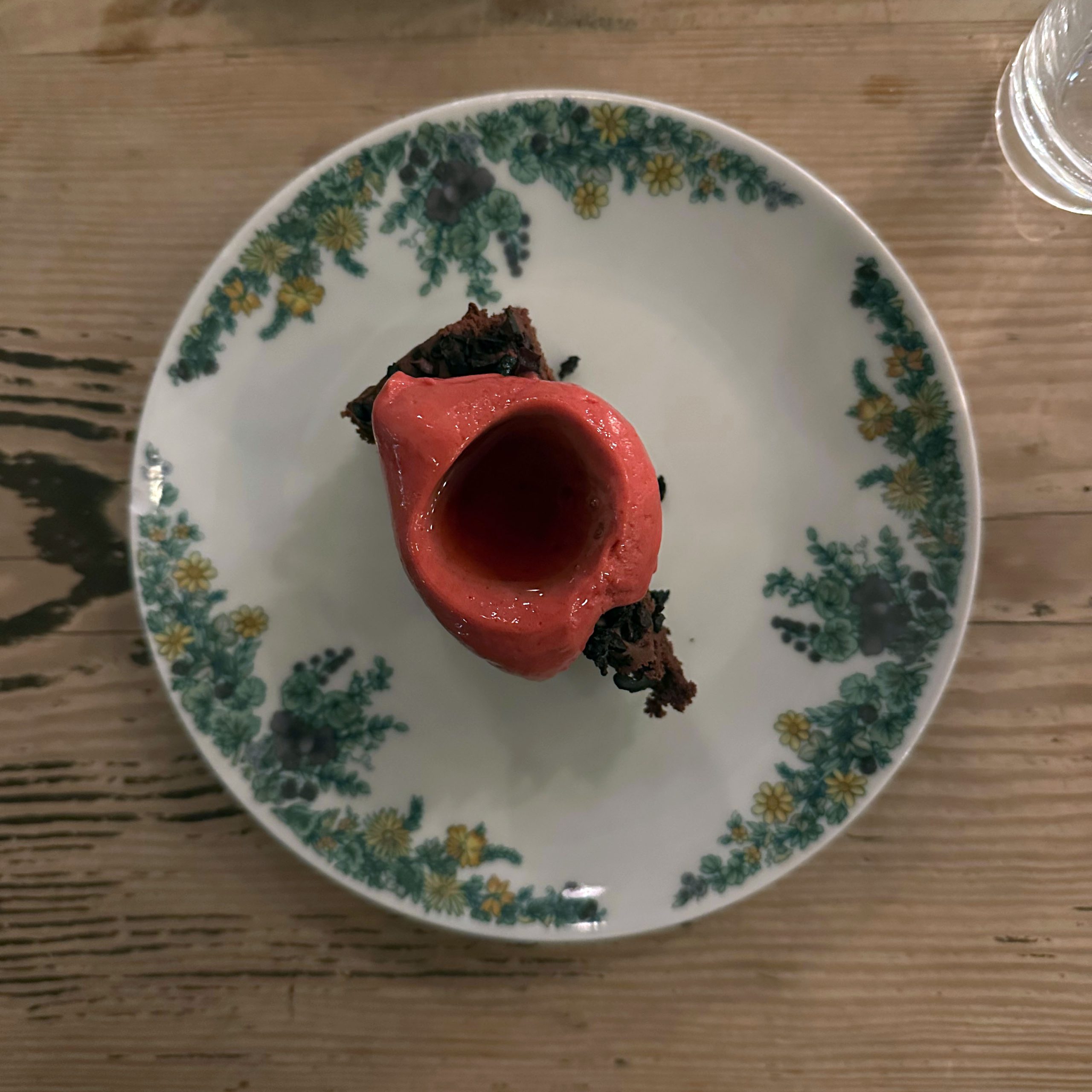 Schokoladentorte mit Sauerkirschsorbet auf einem Vintage-Teller mit grünem Blumen- und gelbem Blütenmuster, serviert auf einem Holztisch im Restaurant Michelberger.