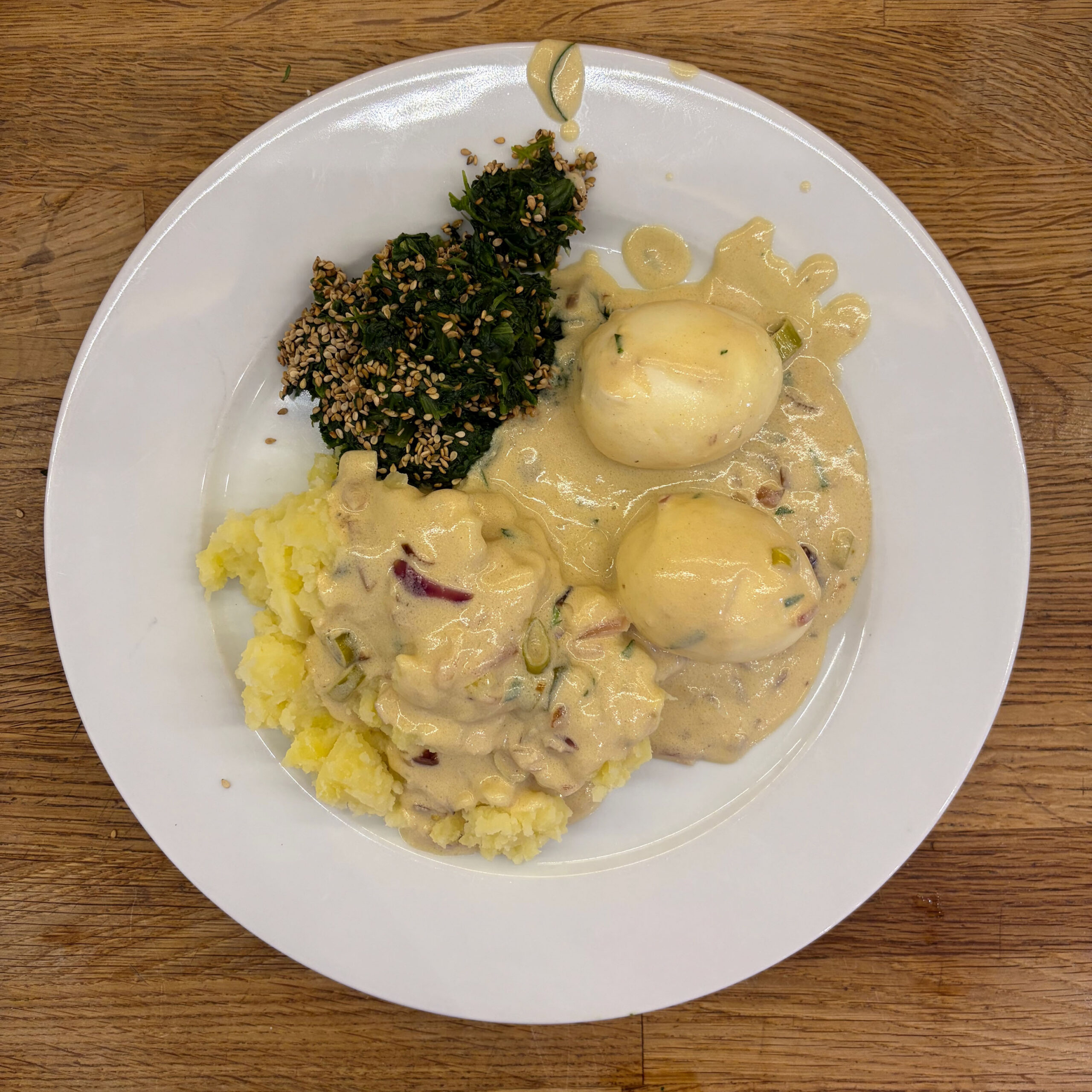 Teller mit Senfeier in cremiger Senfsoße mit Lauchzwiebeln, serviert neben gelbem Kartoffelpüree und gehacktem Spinat mit Sesam.