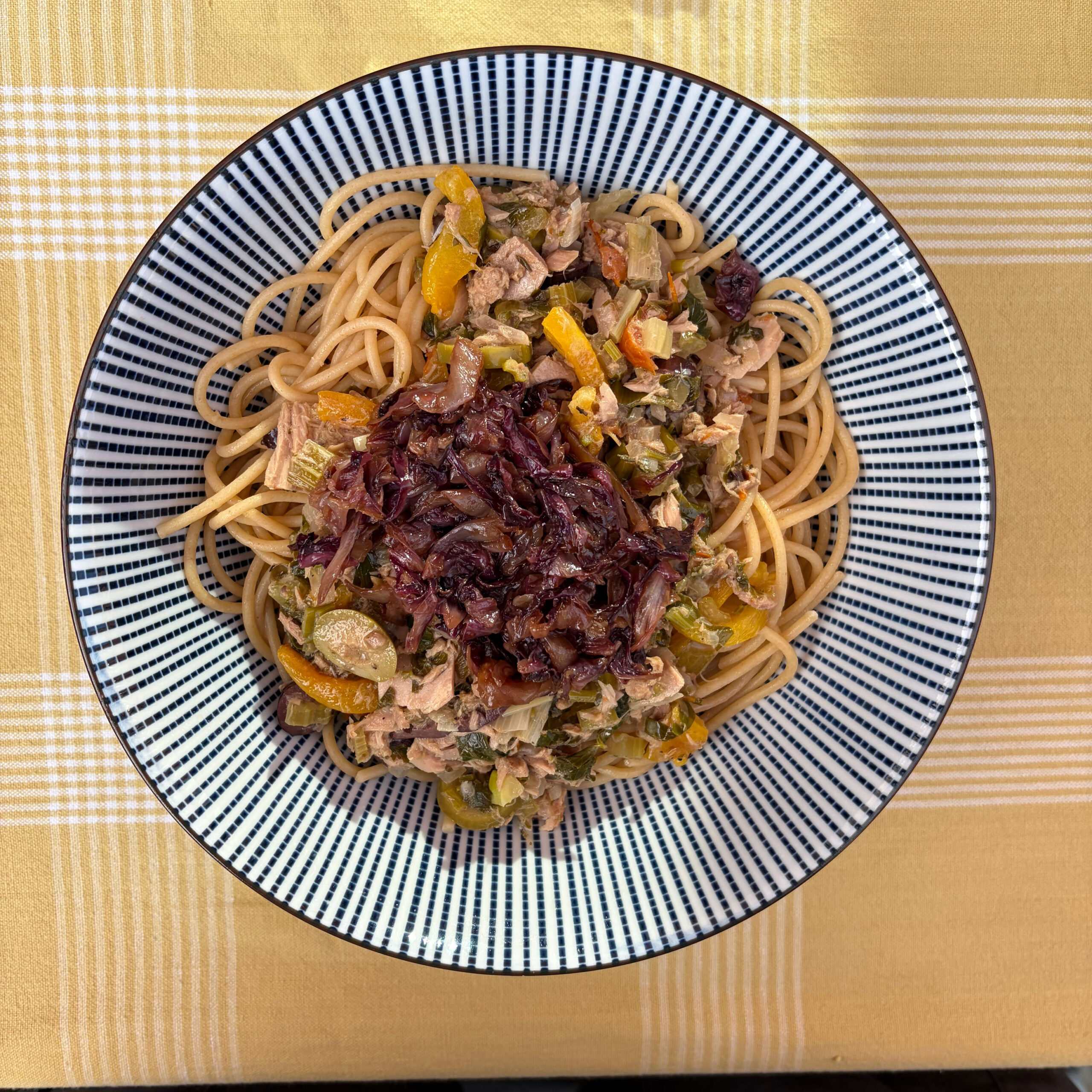 Teller mit Vollkornspaghetti, belegt mit einer Thunfisch-Sellerie-Soße aus getrockneten Tomaten, Kapern, Oliven und Hafersahne, garniert mit gebratenem, mariniertem Radicchio.