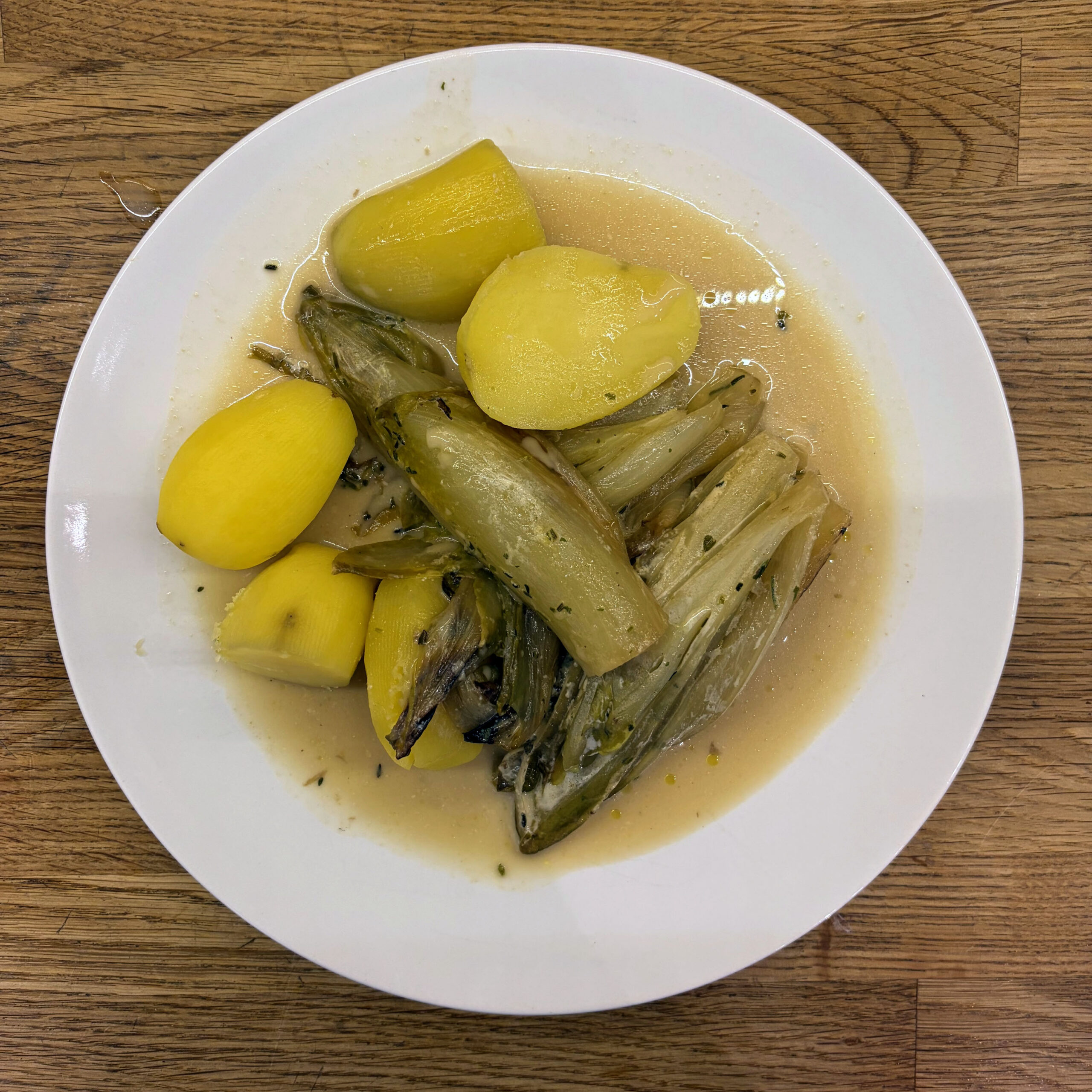 Gebratener und gekochter Chicorée in hellbrauner Mandelsahnesauce mit ganzen, gekochten Kartoffeln auf einem weißen Teller, von oben fotografiert.