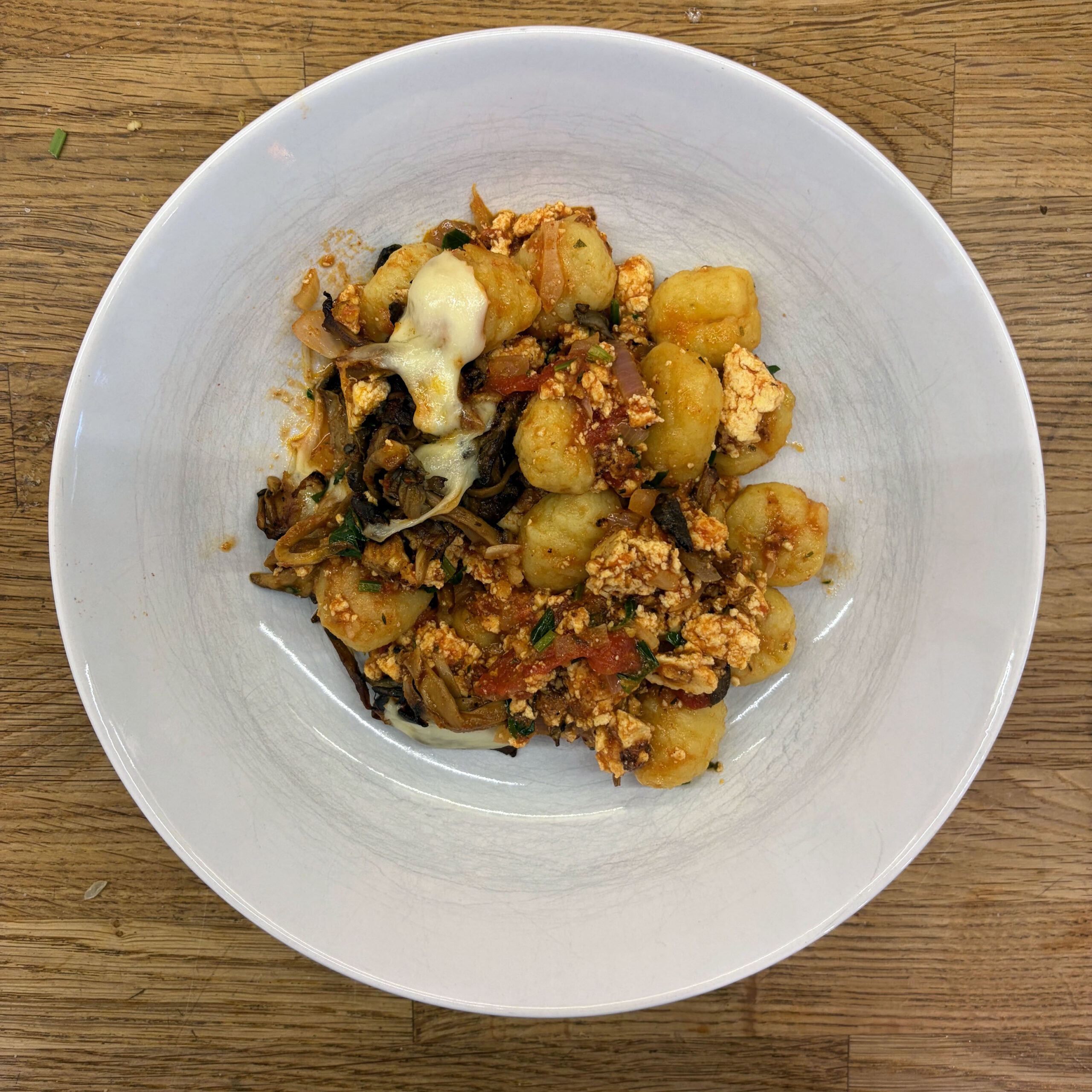 Gnocchiauflauf mit Tofubolognese, gebratenen Austernpilzen und geschmolzenem Mozzarella in einer weißen Schüssel, von oben fotografiert.