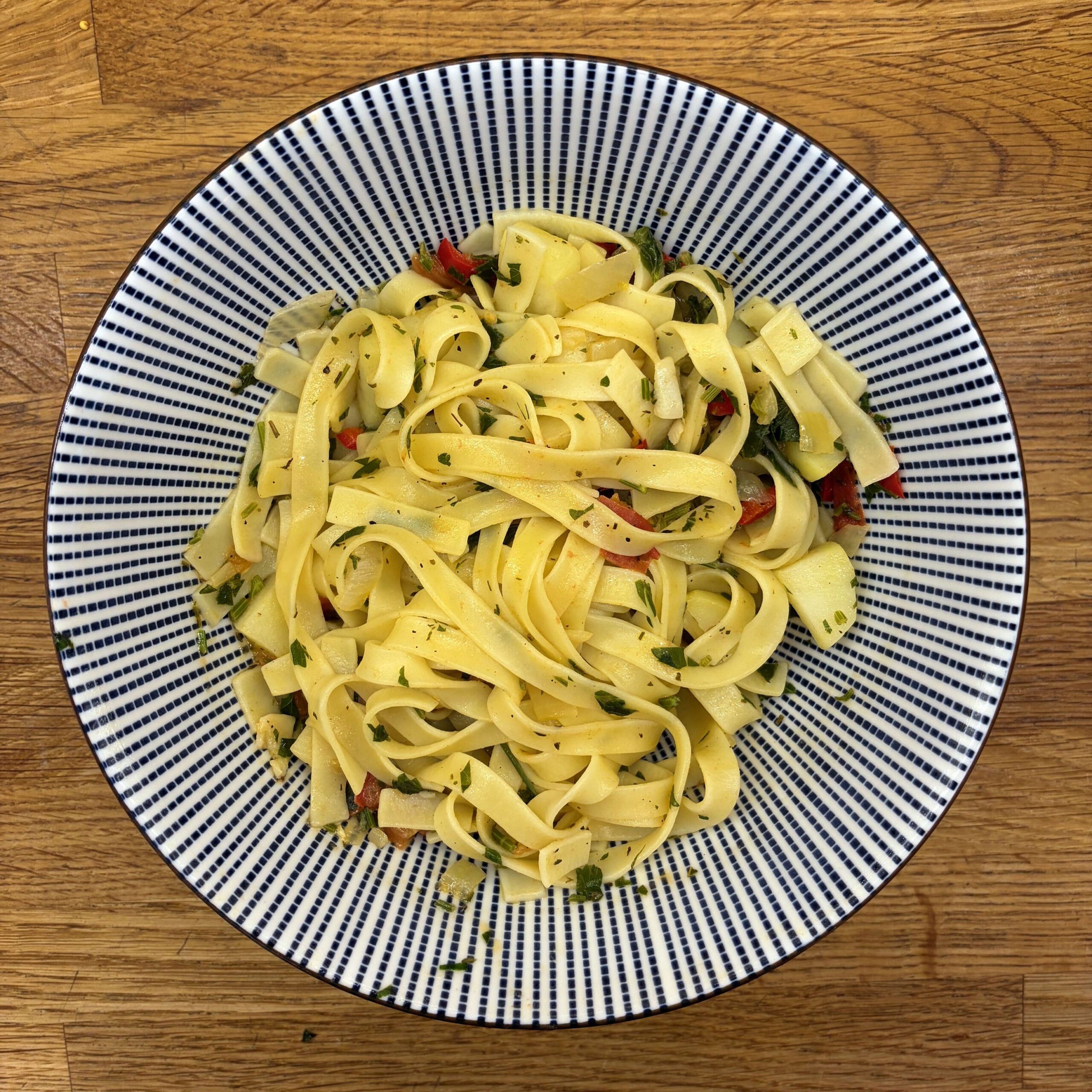 Tagliatelle mit Knoblauch, Chili und Petersilie auf einem blau-weiß gestreiften Teller, serviert auf einem Holztisch.