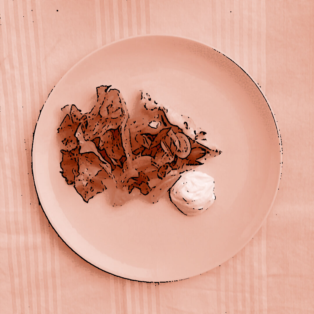 Ein Stück Tomaten-Tarte-Tatin mit karamellisierten Kirschtomaten, Kalamata-Oliven und frischem Basilikum auf einem weißen Teller, serviert mit einem Klecks Ziegenfrischkäse-Dip und grünem Blattsalat. Der Teller liegt auf einem rot-weiß-rosa gestreiften Tischtuch.