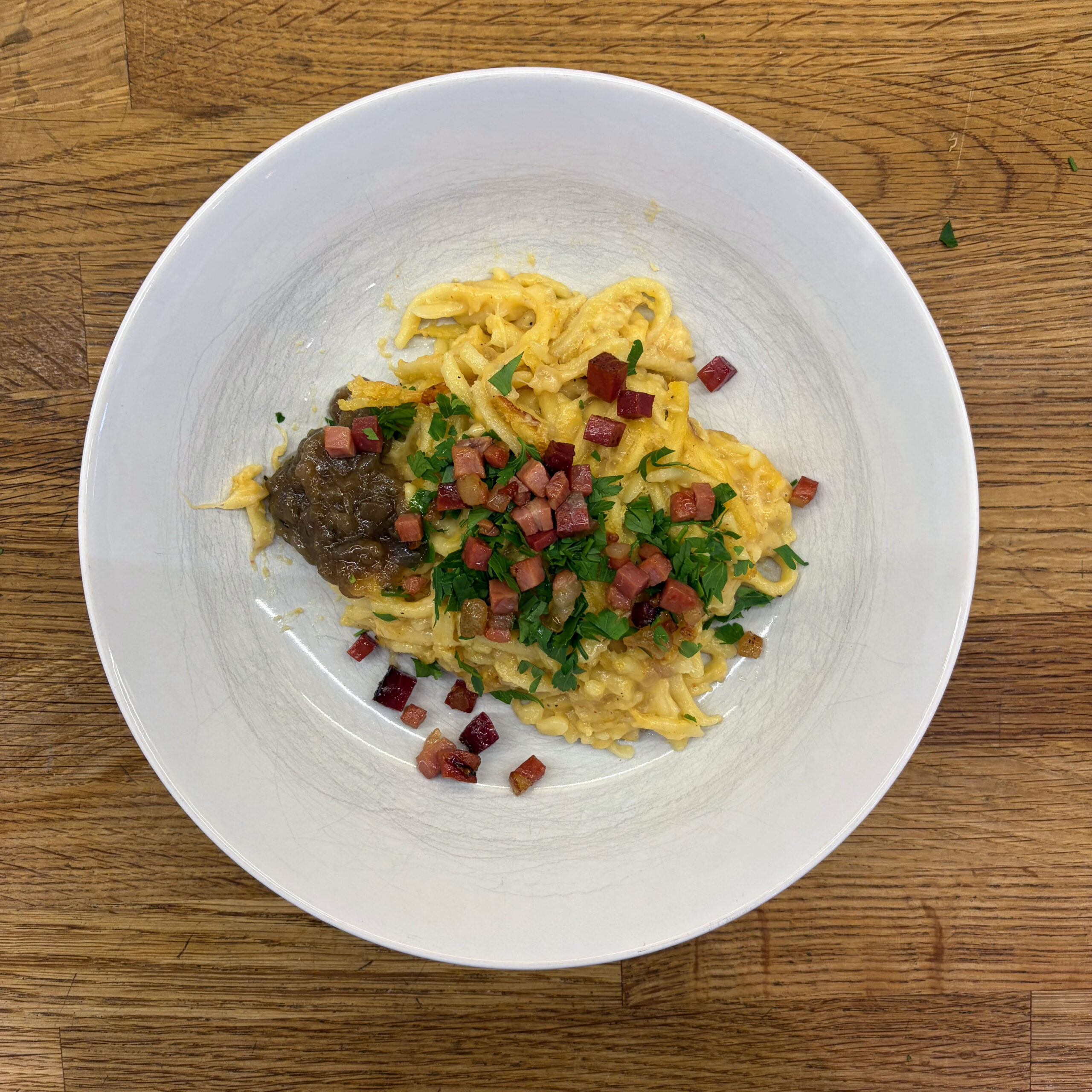 Teller mit Käsespätzle, belegt mit gewürfeltem gebratenem Speck, gehackter Petersilie und karamellisierten roten Zwiebeln, serviert mit Weißkrautsalat.