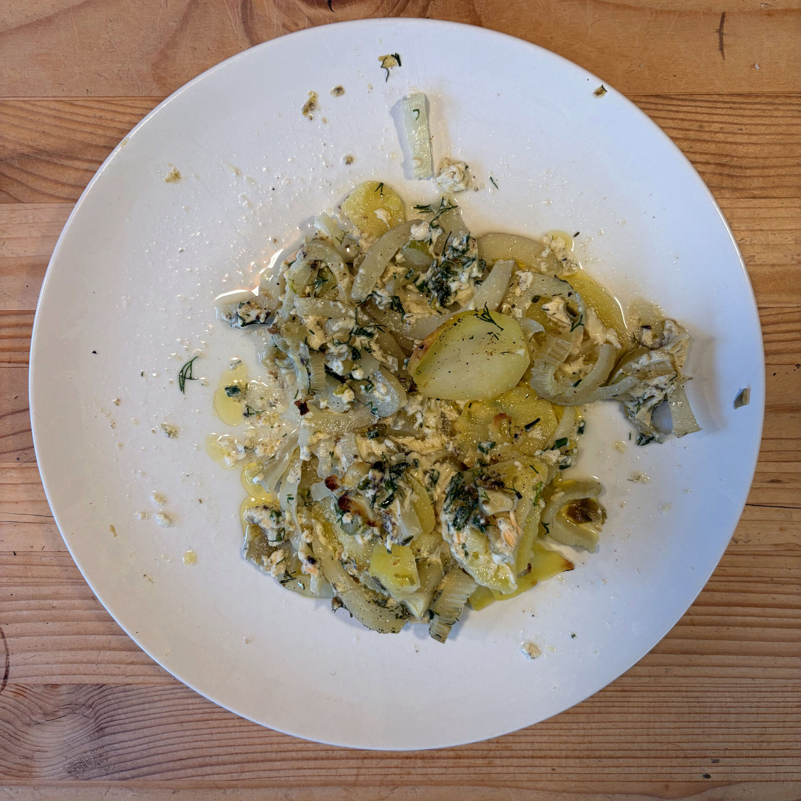 Gekochte Kartoffel- und Fenchelscheiben mit zerkrümeltem Feta, Dill und Olivenöl auf einem weißen Teller – Reste eines Kartoffel-Fenchel-Gratins mit Lachs.
