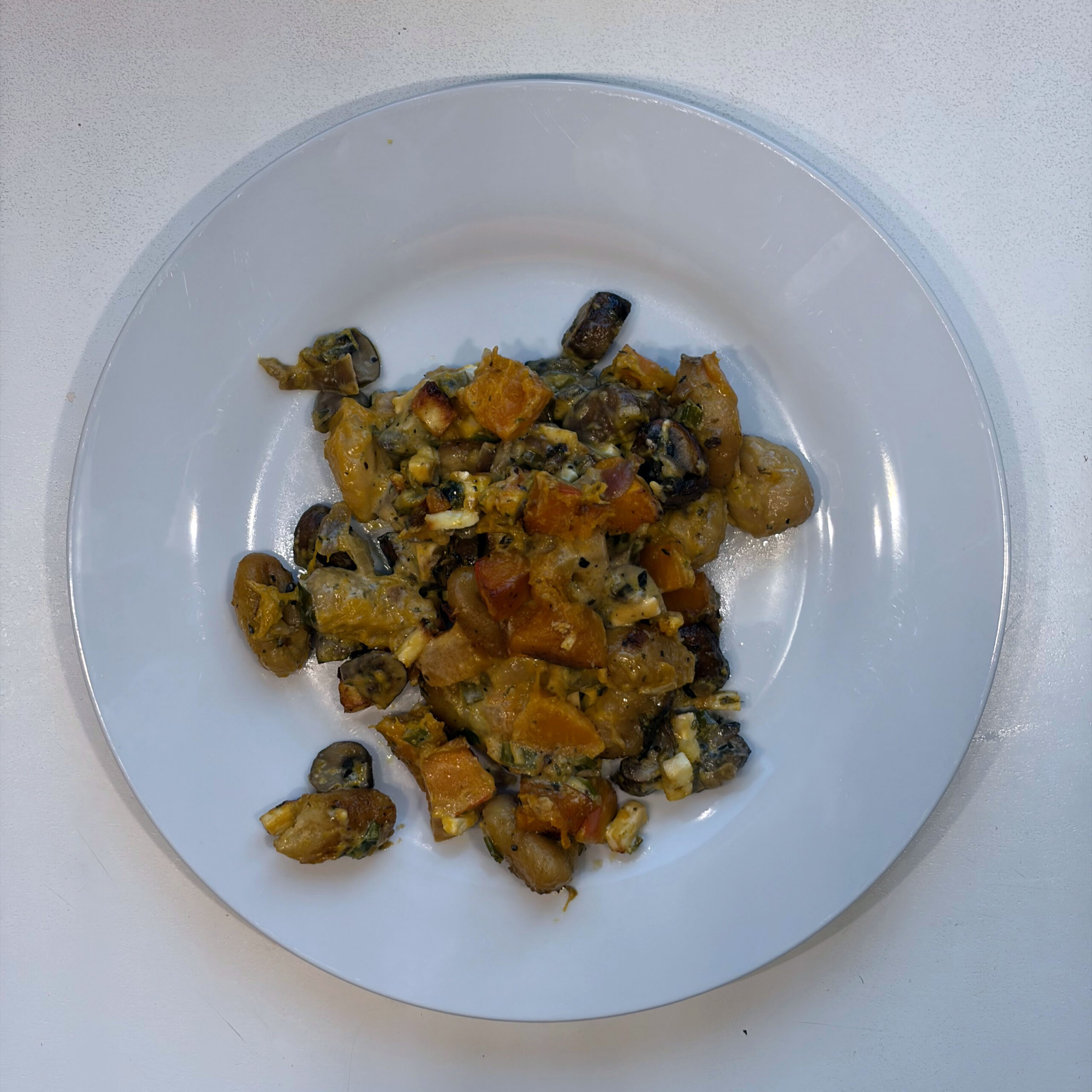 Teller mit Gnocchi-Auflauf, bestehend aus gebackenen Gnocchi, gewürfeltem Ofenkürbis und gebratenen Champignons in cremiger Kräuter-Sahnesoße mit Feta.