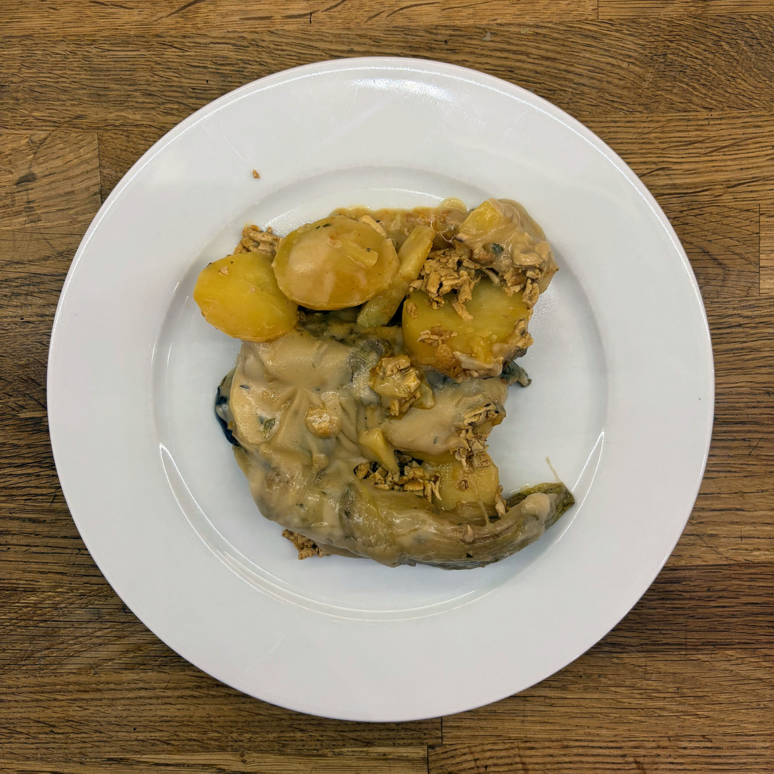 Weißer Teller mit veganem Chicorée-Auflauf: gedünsteter Chicorée und Kartoffelscheiben, bedeckt mit cremiger Béchamelsauce und geröstetem geriebenem Tofu.